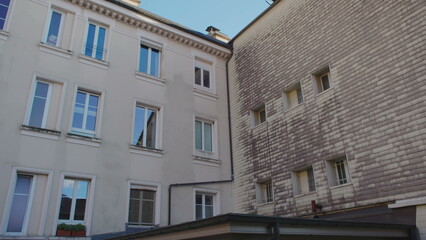 Obraz premium Exterior View of Residential Building Facades Under Clear Sky Showing Windows Architectural Details and Urban Texture in Quiet Neighborhood Setting