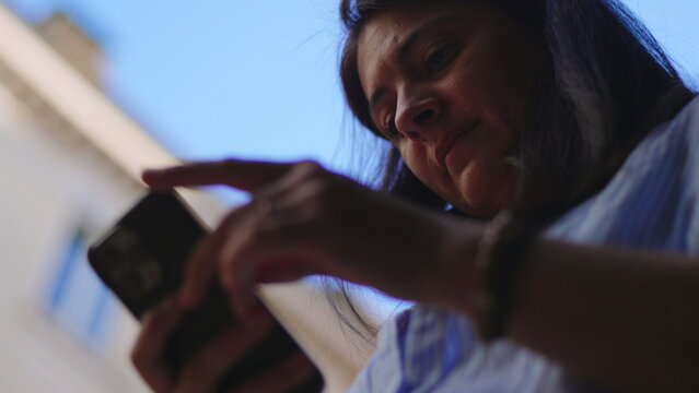 Woman holding smartphone outside while tapping and swiping screen with focused expression creating relaxed moment of digital engagement connection and everyday interaction