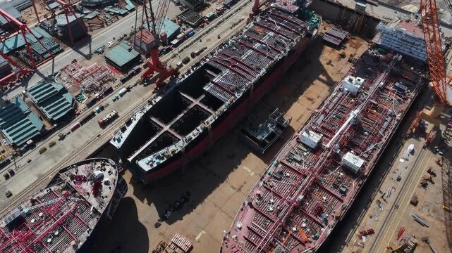 Shipyard construction site featuring large ship hull sections under assembly with cranes and workers