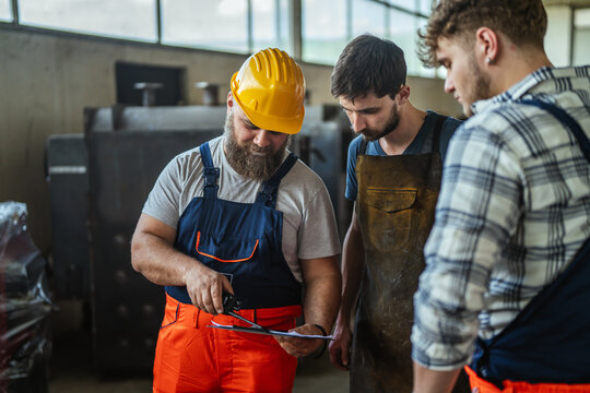 Experienced engineers mentoring young apprentices in industrial factory workplace