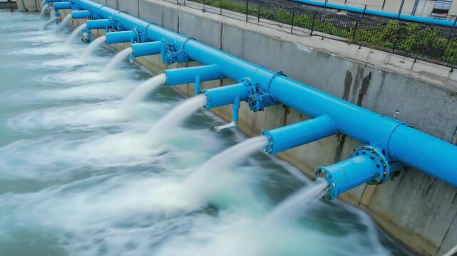 Multiple industrial blue pipes discharging large volumes of water into a pool for water management, utility concept