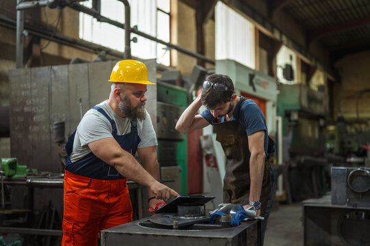 Experienced worker mentoring junior employee in factory workshop