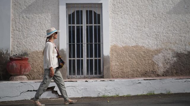 A mature woman explores San Ignacio in Baja California Sur, walking past the historic mission and local buildings on a sunny day.