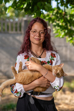 Young woman holding orange tabby cat in sunlit garden