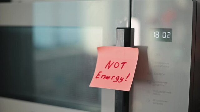 A hand reaches to place a sticky note on a refrigerator door, signaling a reminder regarding energy use