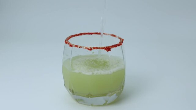 Pouring of grape and mousambi juice in a glass with salt and red chilli powder at the rim of the glass