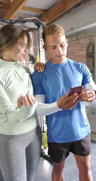 Vertical video: Diverse couple leaning in scrolling phone and checking routine in home gym