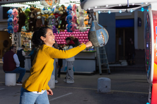 Young Hispanic woman punching boxing machine at carnival