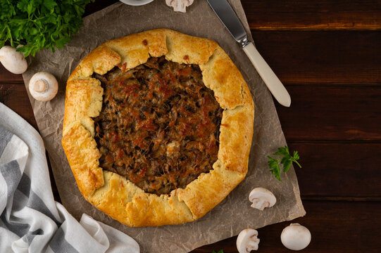 Savory galette or open pie with mushroom, onion and cheese on a dark wooden background. Rustic style. Top view.