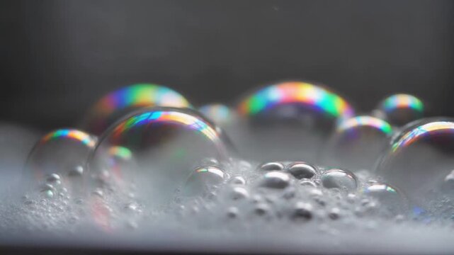 Close up slow motion water pouring onto rainbow soap bubbles creating foam