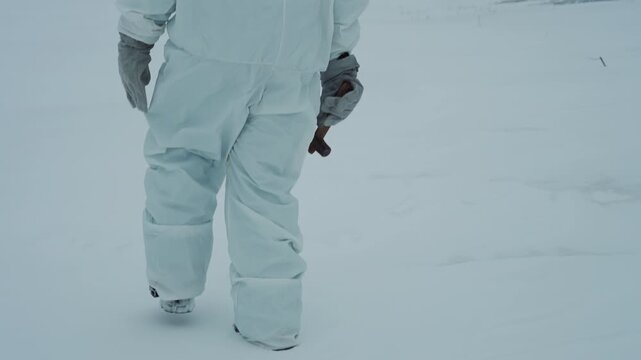 Scientist hazmat suit walking across frozen river toward distant reactor building, close footprints in snow, gloved hand holding sampling kit, overcast sky, cold palette evoking postapocalyptic