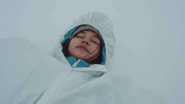 Woman in protective suit lying on snowcovered ground, closeup of researcher in white coverall and hood with frosty lashes, subtle nuclear hazard undertone, scattered scientific gear halfburied, pale