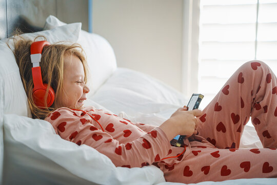  Leisure concept. Happy girl listening to music in headphones, chatting on her smartphone