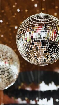 Vertical video of hanging disco balls in a wedding setting. Silver mirror balls with sparkling reflections. No people and no food. Focused on cinematic party atmosphere in 4K slow motion.