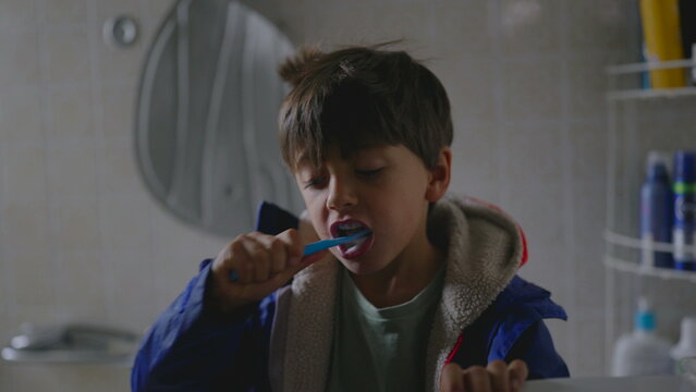 Young boy brushing teeth in bathroom before school creating calm morning moment showing early independence hygiene routine and focused preparation as part of everyday family start to the day