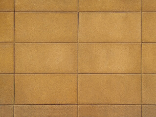 Fototapeta premium Wall of pressed concrete blocks or rectangular cobblestones with rough texture in yellowish beige or sandy yellow tone. Facade cladding surface, exterior paving, dividing and party fence background.