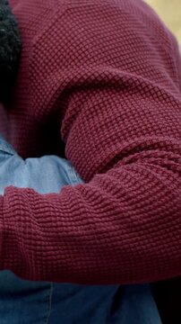 Vertical video: Wrapping arm, dad calming child in park, child leaning in, maroon sweater, watch