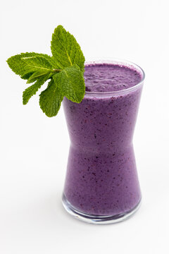 Fresh blueberry smoothie in glass with mint leaves, healthy purple berry drink. Delicious, cold, and refreshing vegan detox drink for breakfast
