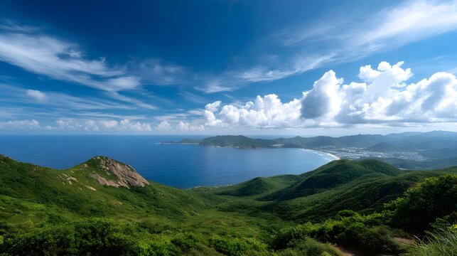 Rolling green hills frame a wide panoramic coastal view meeting the expansive blue ocean under a dramatically cloudy sky