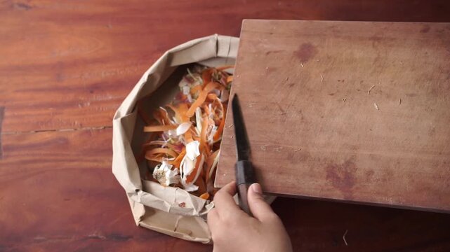 Close up woman hand collecting vegetable scraps into paper bag, sustainability at home concept