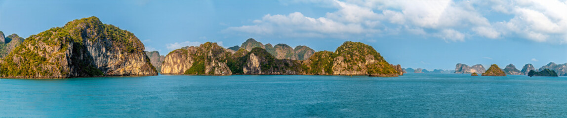 Naklejka premium A panorama view from a cruise ship passing by Karst limestone islets in Ha Long Bay, Vietnam illuminated by the evening light
