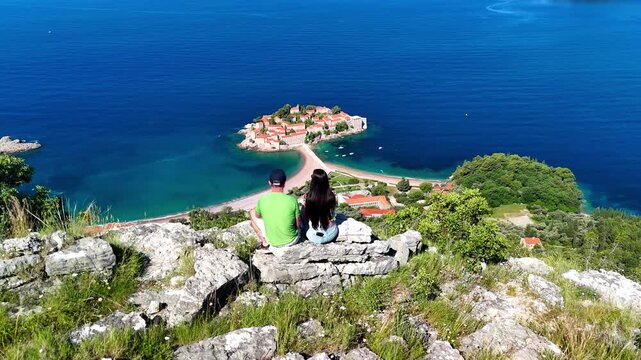 Aerial drone view of Sveti Stefan island and beach in Montenegro, featuring stunning architecture on the Adriatic coast. People enjoy the view.