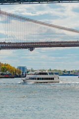 Fototapeta premium White Ferry Passing Beneath Brooklyn Bridge In New York. White passenger ferry crosses East River beneath Brooklyn Bridge cables in New York, daytime.
