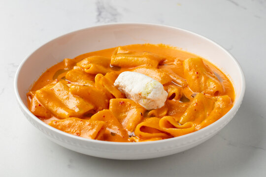 Pasta in creamy tomato sauce topped with sour cream on a white plate
