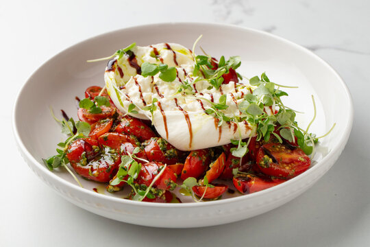 Burrata and tomato salad with balsamic glaze and microgreens on a white plate