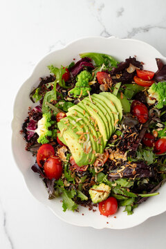 Mixed green salad topped with sliced avocado on white background
