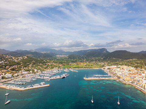 Aerial view of Port d'Andratx harbor with numerous yachts moored in the marina, coastal buildings, and rugged green mountains under a bright sky Port d'Andratx, Balearic Islands, Spain.