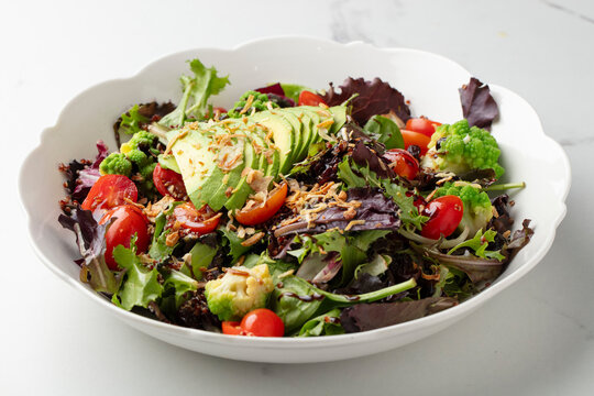 Fresh mixed salad with avocado, cherry tomatoes and greens on white background