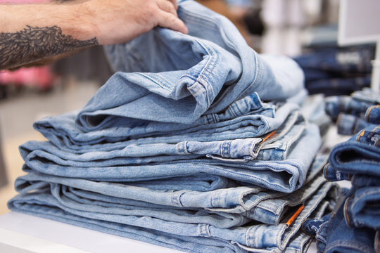 Hand picking light blue jeans from a neatly folded stack in a clothing store, highlighting new denim arrivals and contemporary fashion retail trends with consumer selection