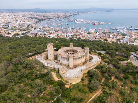 Aerial view of Castillo de Bellver surrounded by pine forest overlooking the city and harbor in Palma, Illes Balears, Spain.