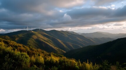 Fototapeta premium Layered mountain ranges viewed under dramatic cloudy skies featuring golden foreground foliage and distant wind turbines