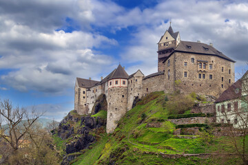 Naklejka premium Medieval Loket Castle on a steep cliff, Czech Republic. Gothic stone fortress under blue sky with white clouds
