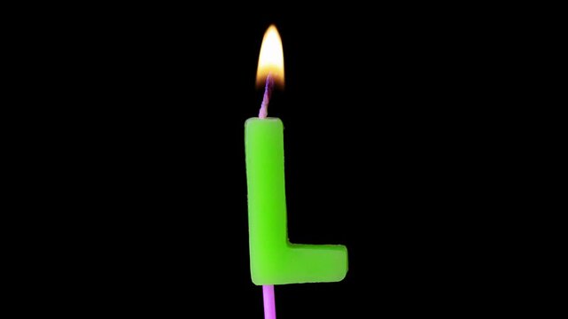 A single green candle in the shape of the letter L with a lit flame on a pink wick against a black background.