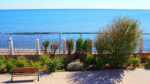 Sunny Seaside Promenade Empty Bench Calm Sea Fishing Boat. Clear Sky Coastal Walkway Bench Blue Sea with Distant Fishermen. Copy space. Background video.