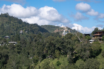Fototapeta premium Mountain town Ella in Sri Lanka. Hotels and houses on a lush green hillside among tropical forest under a blue sky.