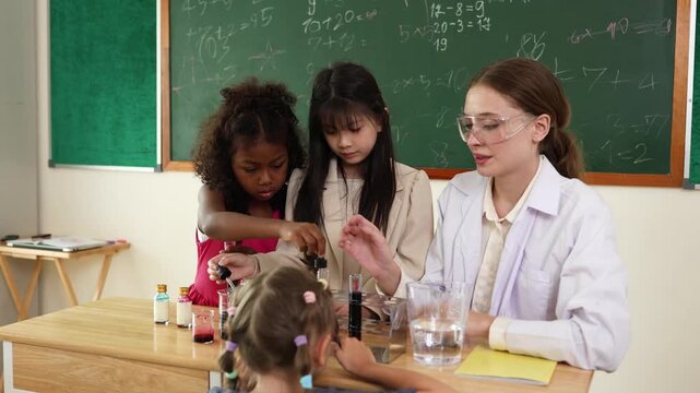 A science teacher guides diverse children in a classroom experiment with test tubes and liquids in front of a chalkboard with math equations.