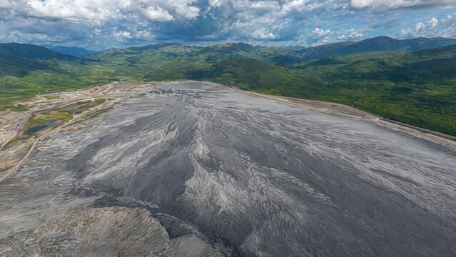 tailings. A vast, fan-shaped field of grey mine tailings contrasting with distant green hills. ESG reports, sustainability campaigns, designed for sustainability communications and ESG reporting.