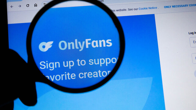Magnifying glass held over the onlyfans logo on a computer screen, concept of online content subscription and digital investigation