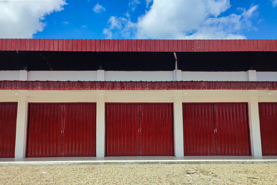 Wide front angle of a long marketplace building featuring symmetrical red metal shutters and white columns. Clean, minimalist architectural style in daylight.