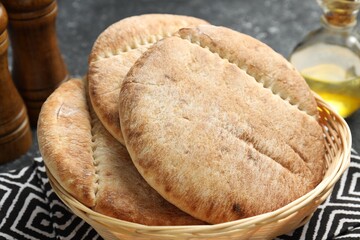 Naklejka premium Fresh pita bread in wicker basket, spices and oil on grey table, closeup