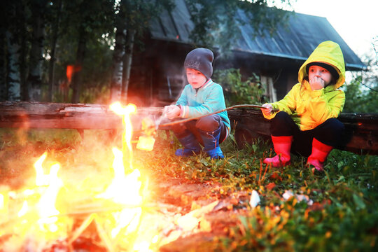 Little children frying marshmallows on bonfire at night. Summer camp