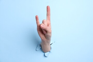 Naklejka premium Woman showing rock gesture through hole in light blue paper, closeup