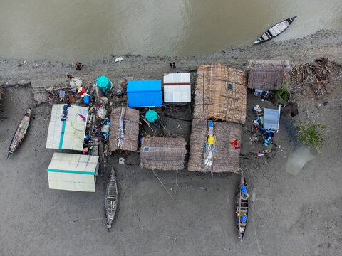 Aerial view of Kalabagi village featuring traditional thatched huts and wooden boats along the muddy riverbank in Khulna District, Khulna Division, Bangladesh.
