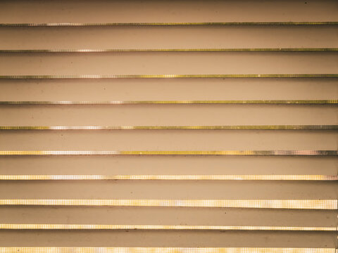 Warm toned abstract close up of horizontal textured slats with glowing light filtering through narrow gaps creating rhythmic geometric patterns