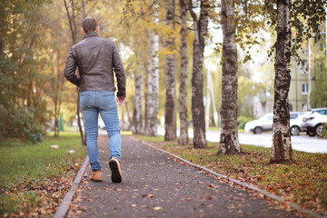 Fototapeta premium Autumn concept. Pedestrian feet on the road. Autumn leaves on the footpath.