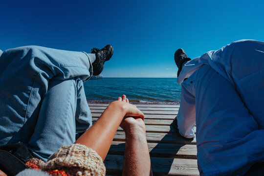 Couple holding hands while relaxing on a wooden pier by the sea